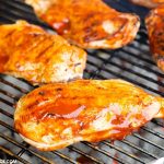 Spicy Jalapeno Popper Grilled Chicken slathered with barbecue sauce as it cooks on a charcoal grill