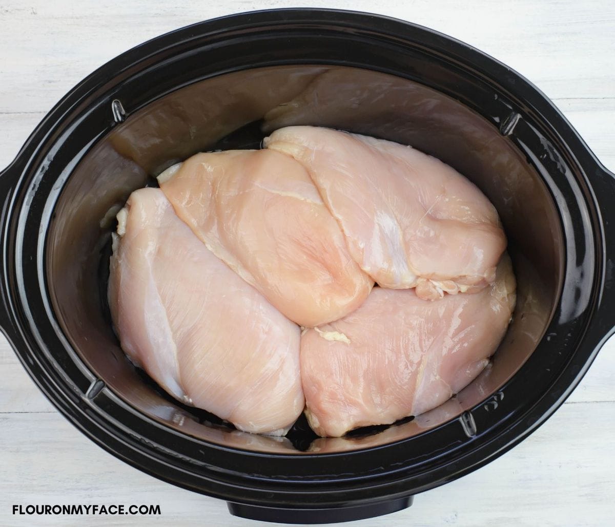 Overhead image of 4 boneless skinless chicken breasts in a crock pot.