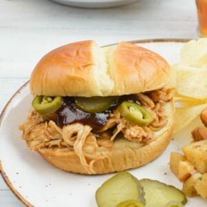 Crock Pot Pulled Chicken Sandwich with sliced pickles and jalapeno peppers on a bun.