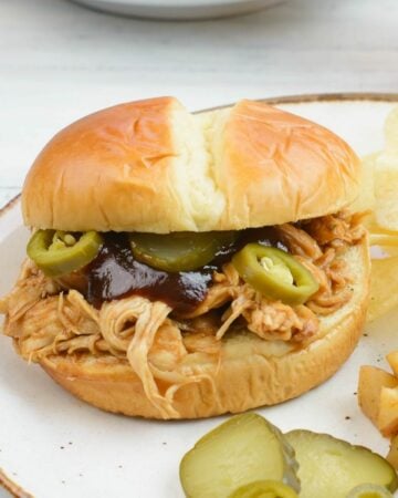Crock Pot Pulled Chicken Sandwich with sliced pickles and jalapeno peppers on a bun.