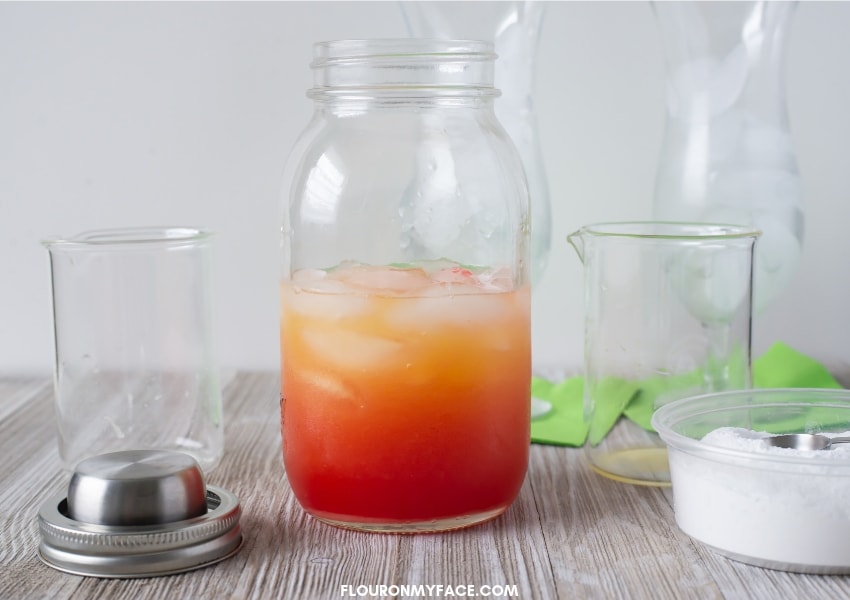 A photo of a Hurricane Cocktail ingredients in a clear mason jar cocktail shaker showing the layers of red and orange when the ingredients are combined before shaking.