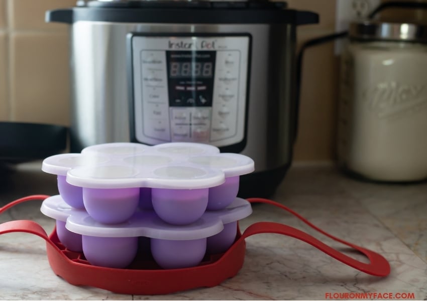 Instant Pot in background with two purple Instant Pot Silicone Egg Bites molds filled with blueberry muffing mix loaded into the silicone sling