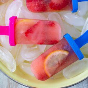 Three strawberry lemonade ice pops in a pie plate on ice cubes.