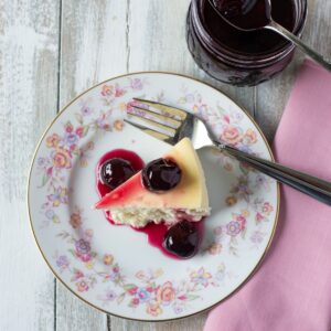 Cherry Preserves drizzled over a slice of cheesecake on a dessert plate.