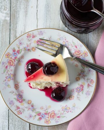 Cherry Preserves drizzled over a slice of cheesecake on a dessert plate.