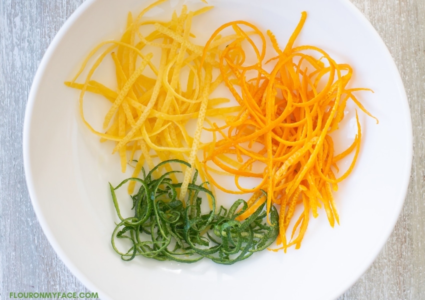 orange, lemon and lime citrus zest in a white bowl.