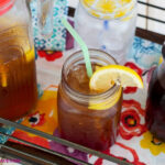 a serving tray with Hibiscus Iced tea in a glass pitcher with a glass next to it filled with ice, hibiscus iced tea with a slice of lemon.