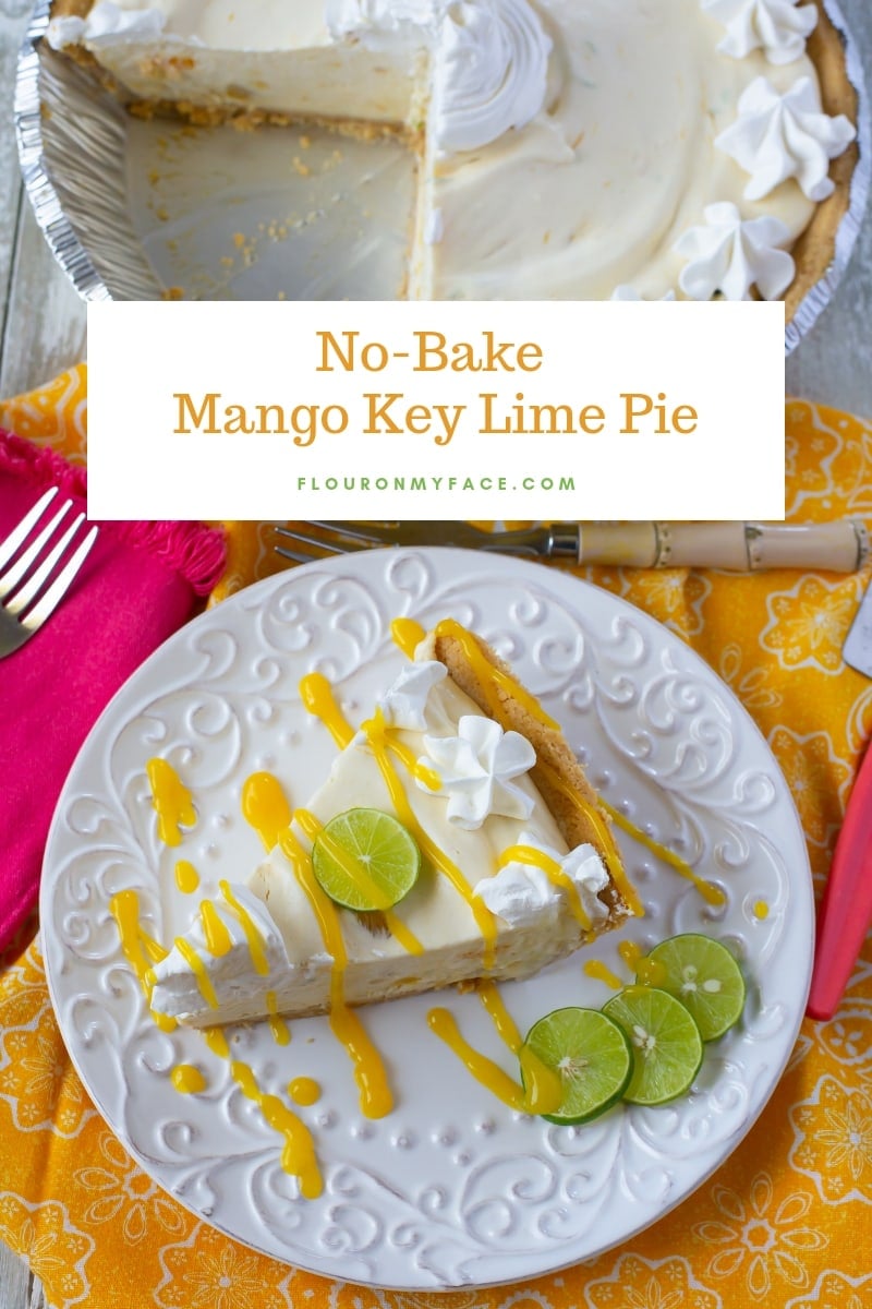 A slice of No-Bake Mango Key Lime Pie with a drizzle of mango sauce, whipped cream and a slice of fresh key lime for a garnish on a white dessert plate . The cut  pie  is in the background.