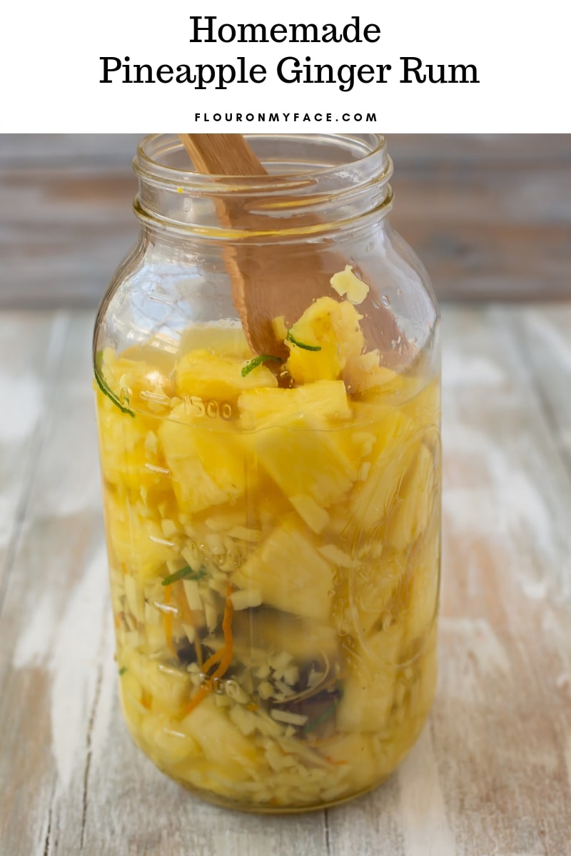 A half gallon mason jar filled with the ingredients to make pineapple ginger rum.