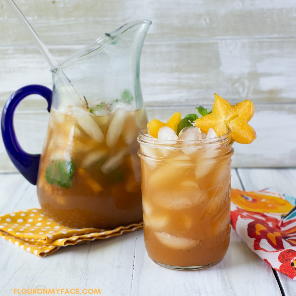 Carambola Iced Tea Cooler in a mason jar with star fruit garnish with a filled pitcher in the background.