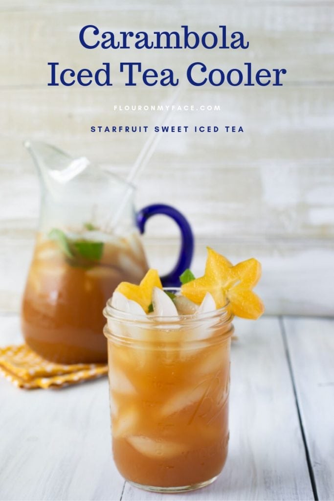 A mason jar glass filled with Carambola iced tea recipe with sliced starfruit and mint garnish. The filled glass pitcher is in the background.