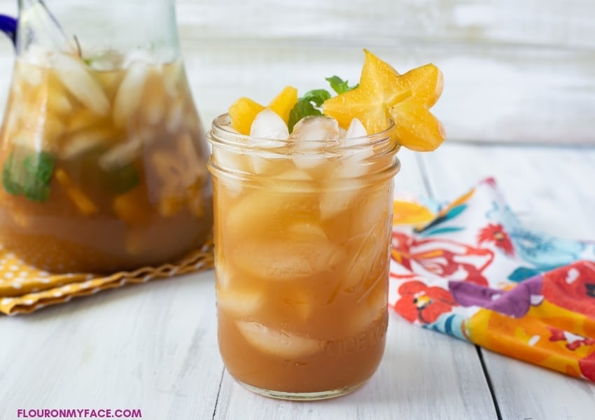 A glass of Carambola Iced Tea Cooler with a serving pitcher full of this tropical drink recipe.