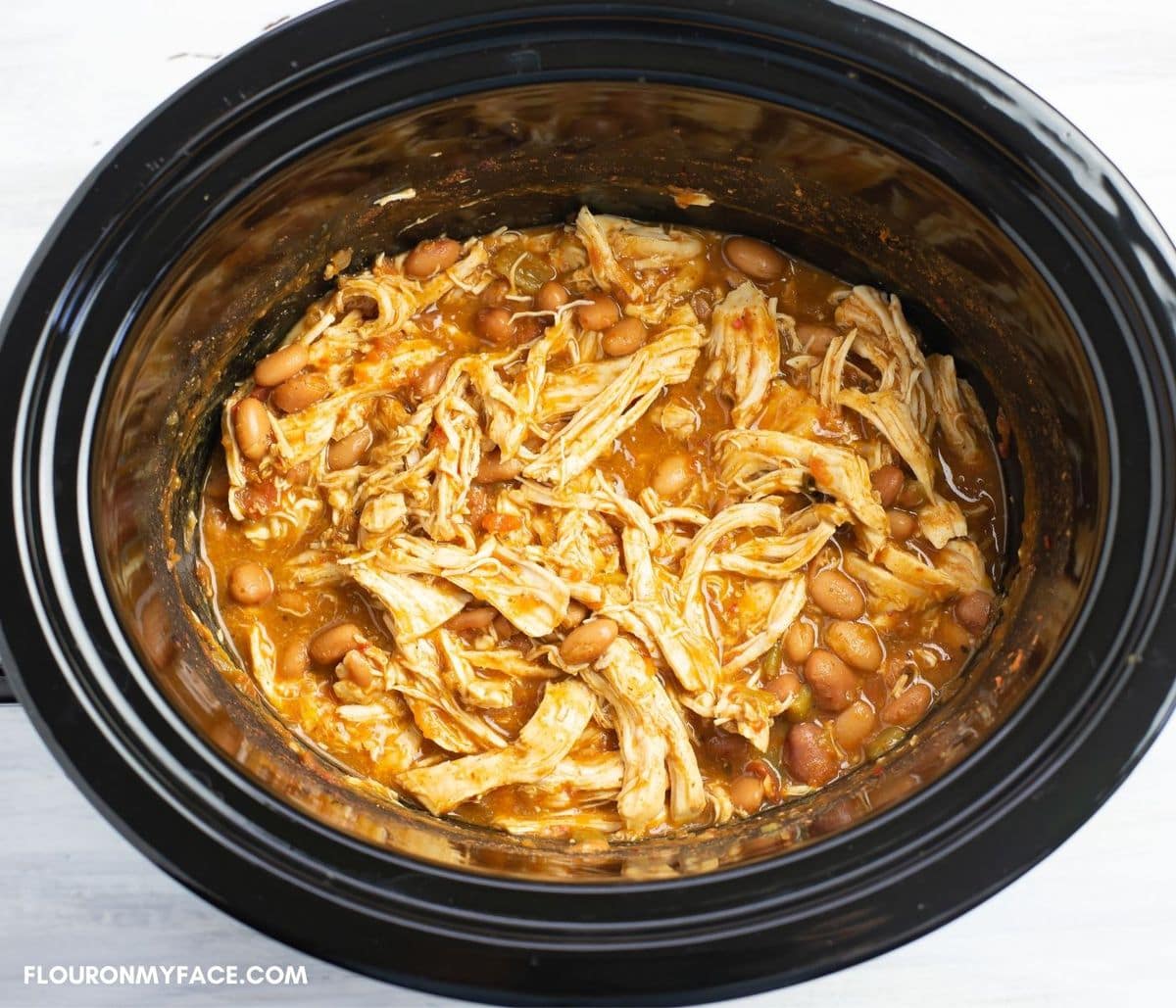 Shredded chicken covered in burrito sauce inside a crock pot.