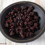a black wooden bowl filled with dehydrated fresh cherries