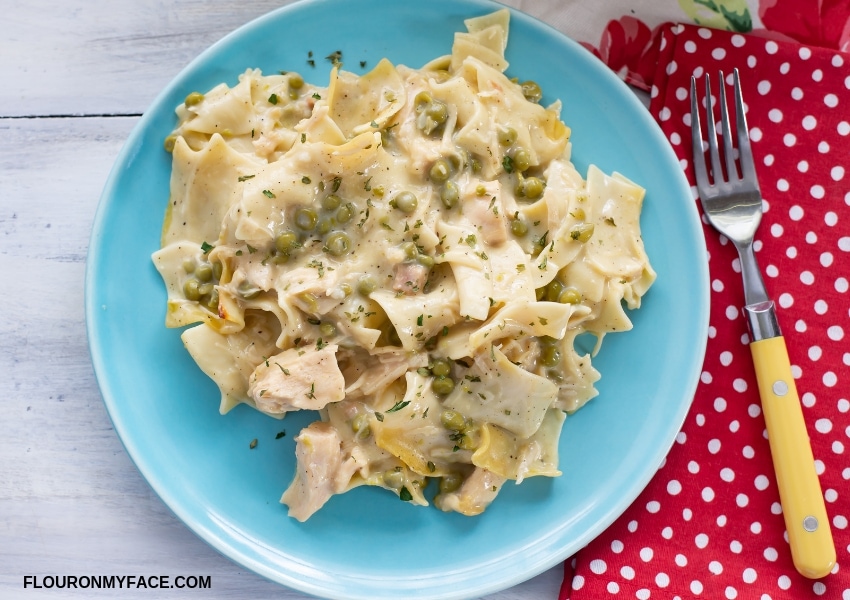 Overhead photo of a blue glass plate with a serving of Chicken Noodle Casserole piled high, with a red and white polka dot cloth napkin in the background.