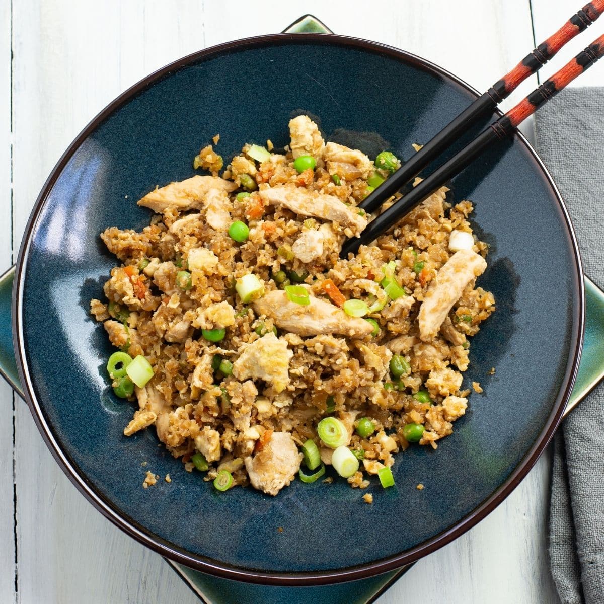 A black glass bowl filled with a serving of low card chicken cauliflower fried rice.