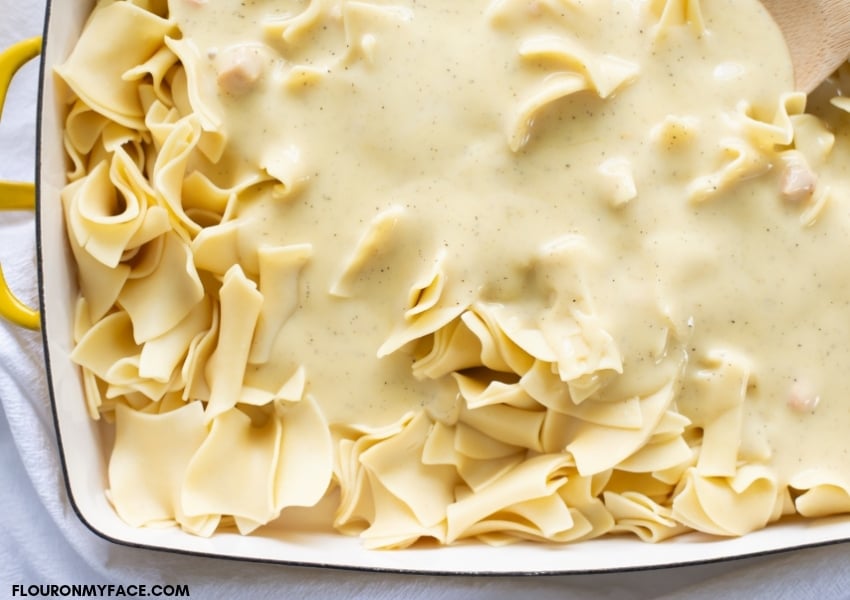 overhead photo of a 9 x 13 baking pan filled with cooked egg noodles with cream of chicken soup poured over the noodles