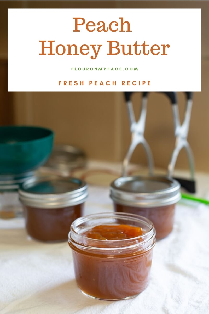 Half pint canning jars and canning equipment on a kitchen counter with one jar in the front that is filled with hot peach honey butter before placing the canning lid on and hot water bath canning.