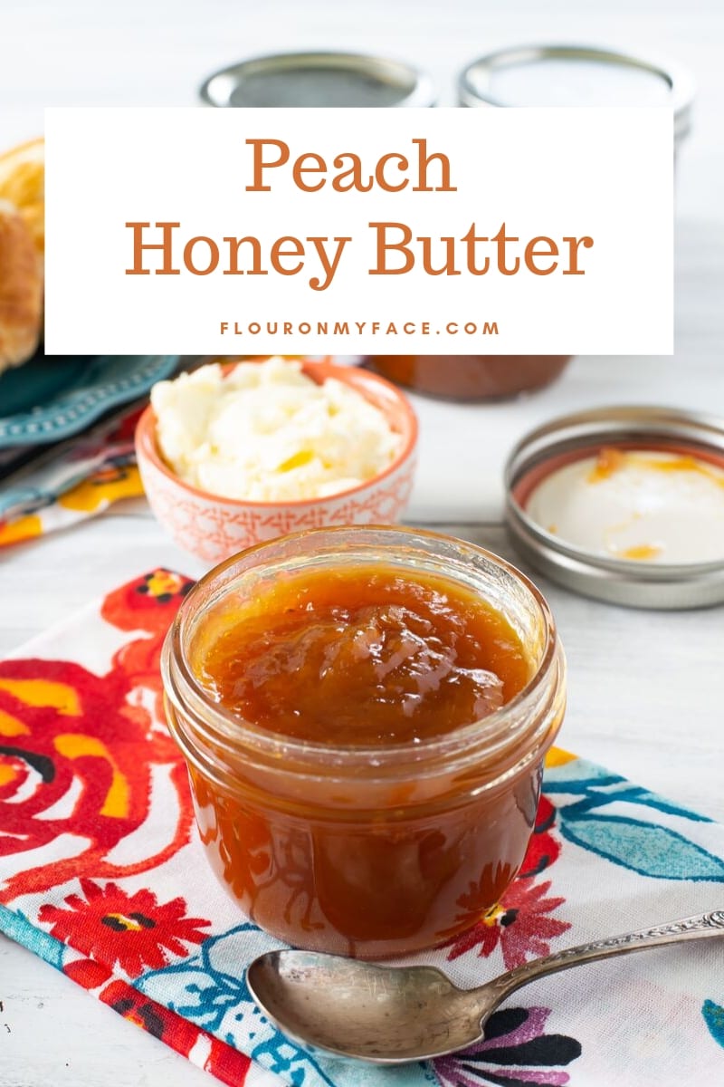 Close up photo of a canning jar filled with homemade Peach Honey Butter on a colorful cloth napkin on the table with a bowl of butter in the background.