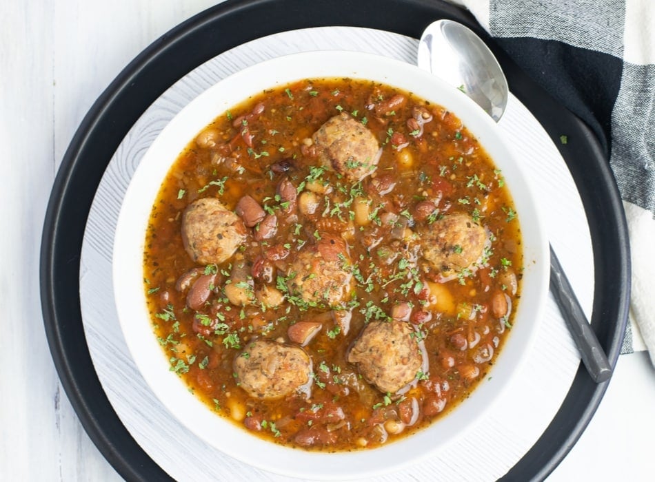 Overhead closeup photo of a white bowl filled with Crock Pot Italian Bean Meatball Soup recipe.