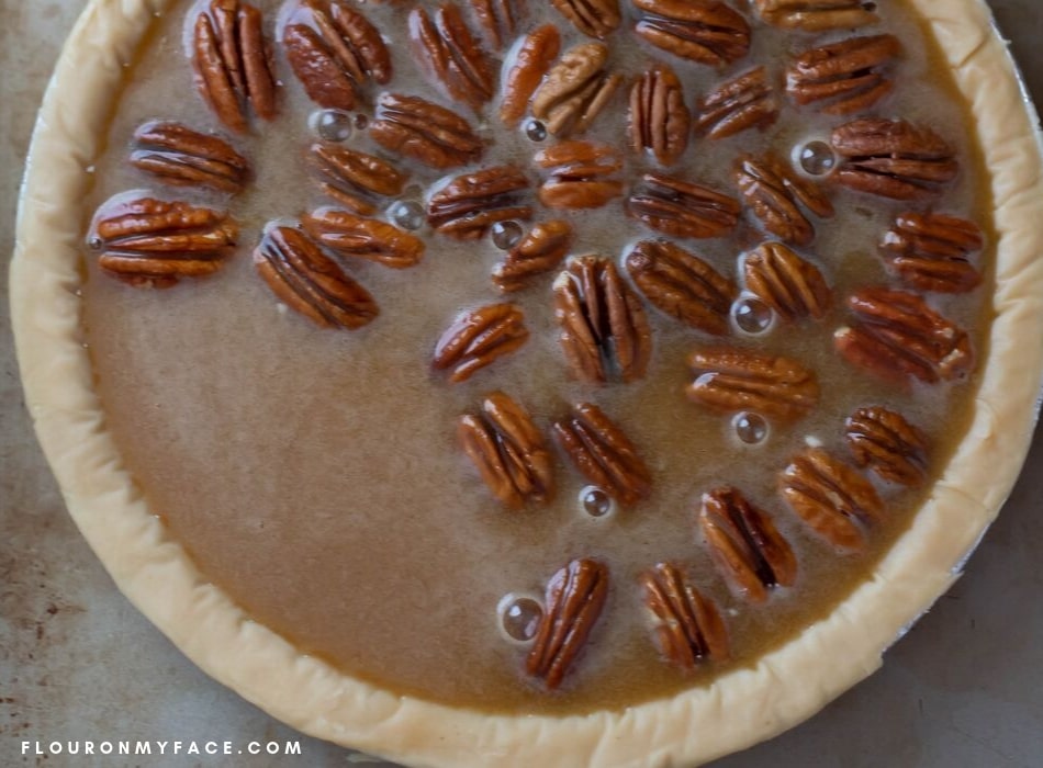 Overhead photo of makings a homemade pecan pie after pouring the filling into the pie shell and watching the pecans float to the top.