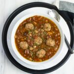 A white bowl filled with Italian Bean Meatball Soup.