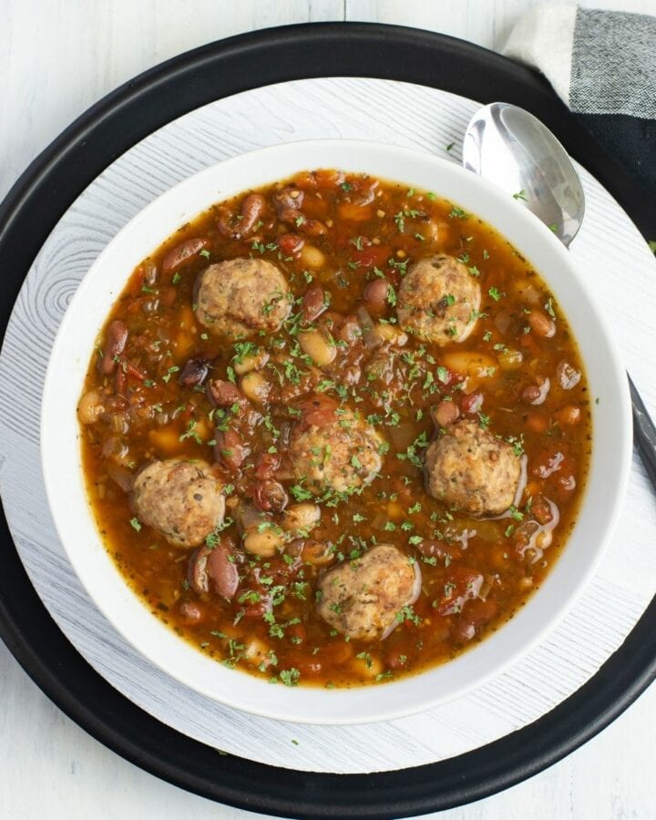 A white bowl filled with Italian Bean Meatball Soup.