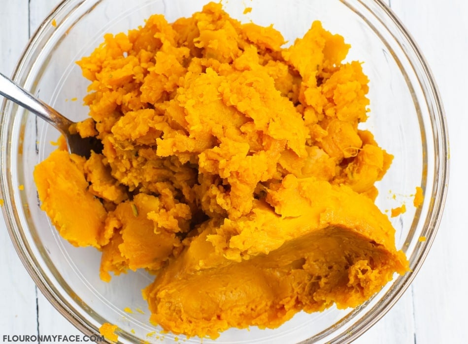 overhead photo of a clear glass bowl filled with the bright orange flesh of a Kabocha squash. Mashed Kabocha squash