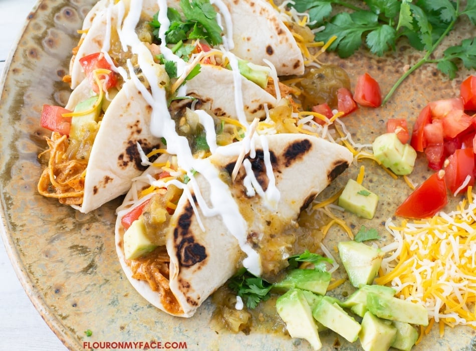 closeup photo of 3 Instant Pot Creamy Chicken Tacos on a plate with taco toppings.