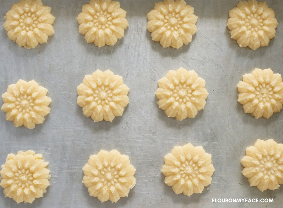 over head photo of pressed Sprtiz cookies shaped like a flower on a aluminum baking sheet before they go in the oven.