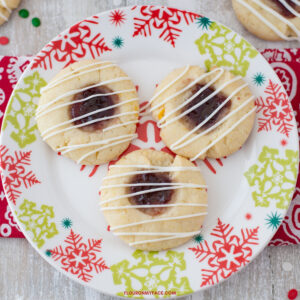 A holiday plate with 3 Raspberry Thumbprint cookies with a white chocolate drizzle.