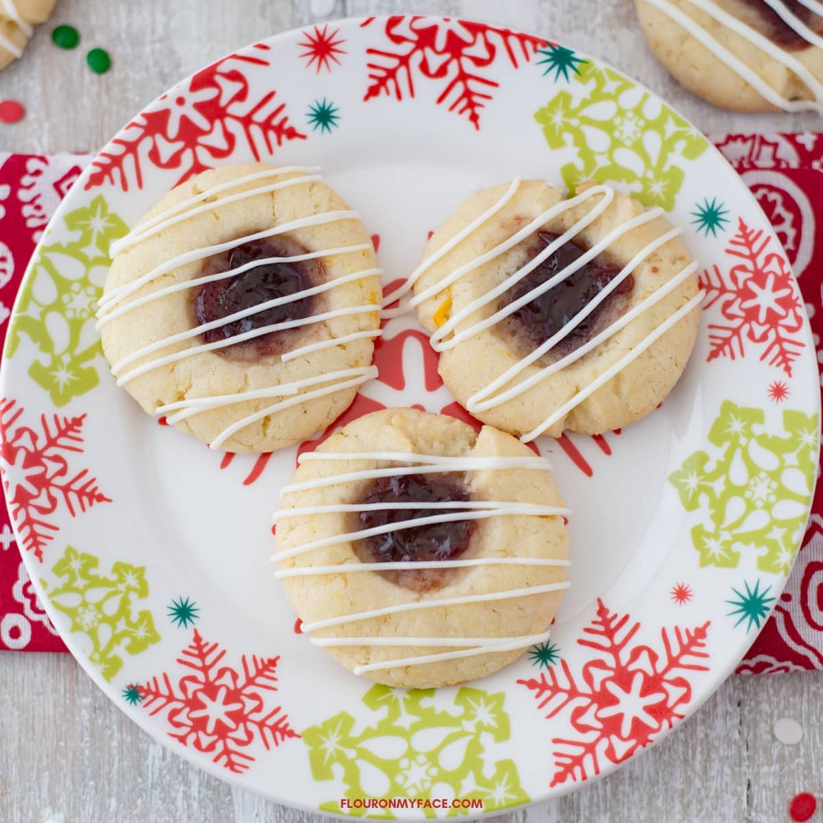 A holiday plate with 3 Raspberry Thumbprint cookies with a white chocolate drizzle.