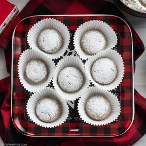 A black and red plaid Christmas plate with homemade German Spice Cookies in muffin papers on a Chrstmas dessert table.
