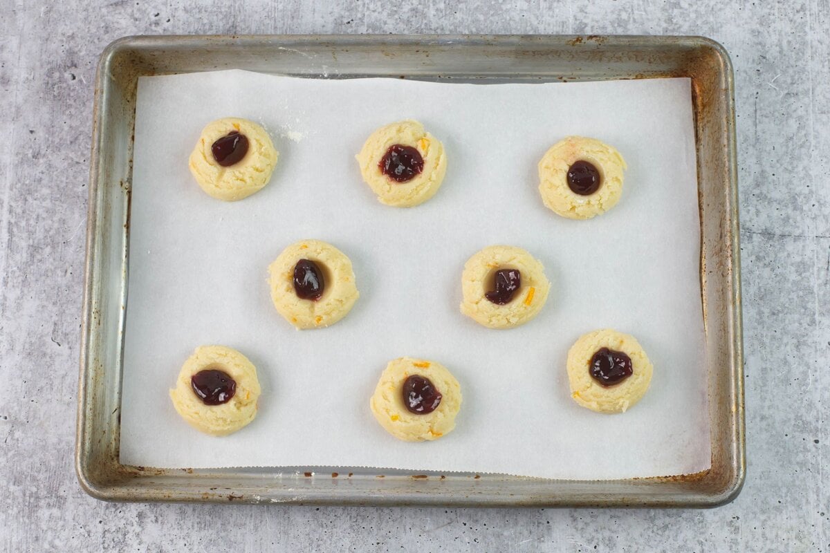 Cookie dough filled with raspberry jam on a baking sheet.