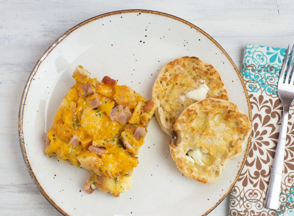 A serving of the Crock Pot Ham, Egg and Cheese Casserole on a plate with a toasted English Muffin