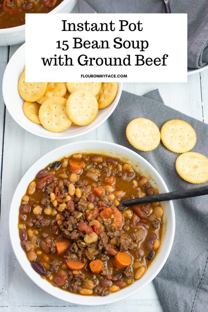 A white soup bowl filled with Instant Pot 15 Bean Soup recipe made with ground beef. A bowl of crackers and a grey cloth napkin are also on the table.