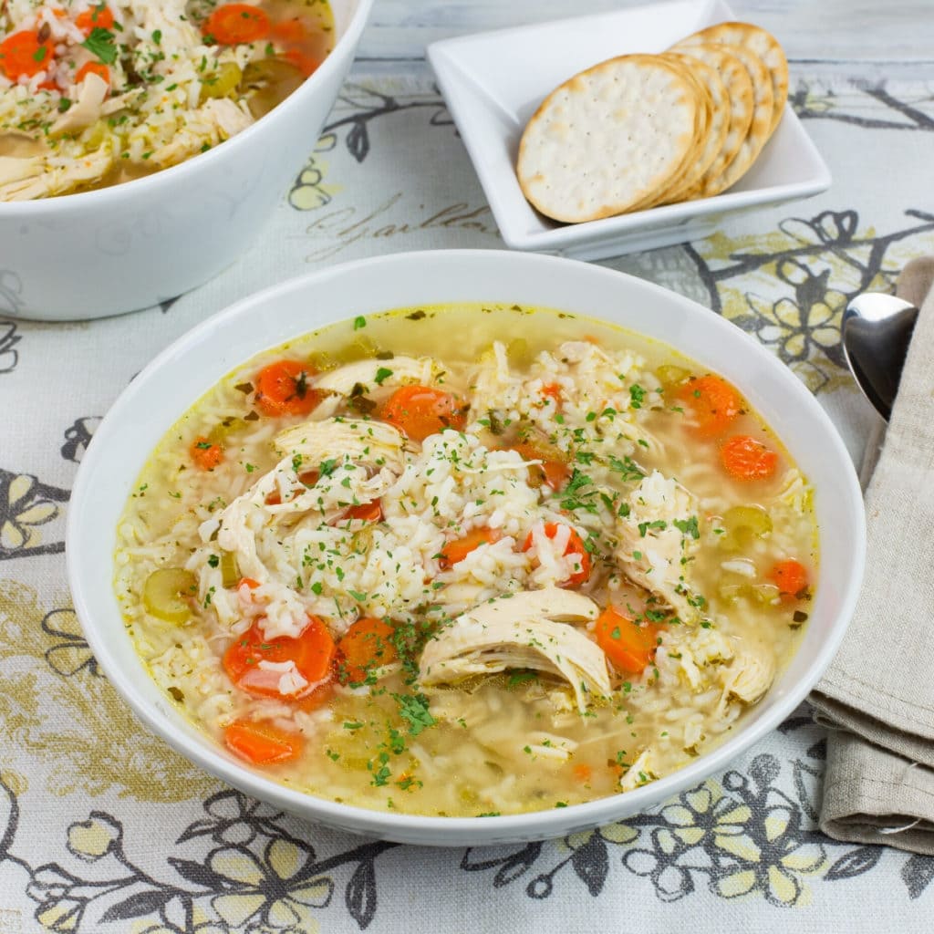 a bowl of Instant Pot Chicken and Rice Soup on a linen place mat with a bowl of crackers
