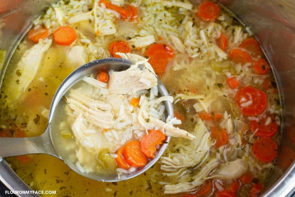 A closeup photo of a ladle full of chicken and rice soup.