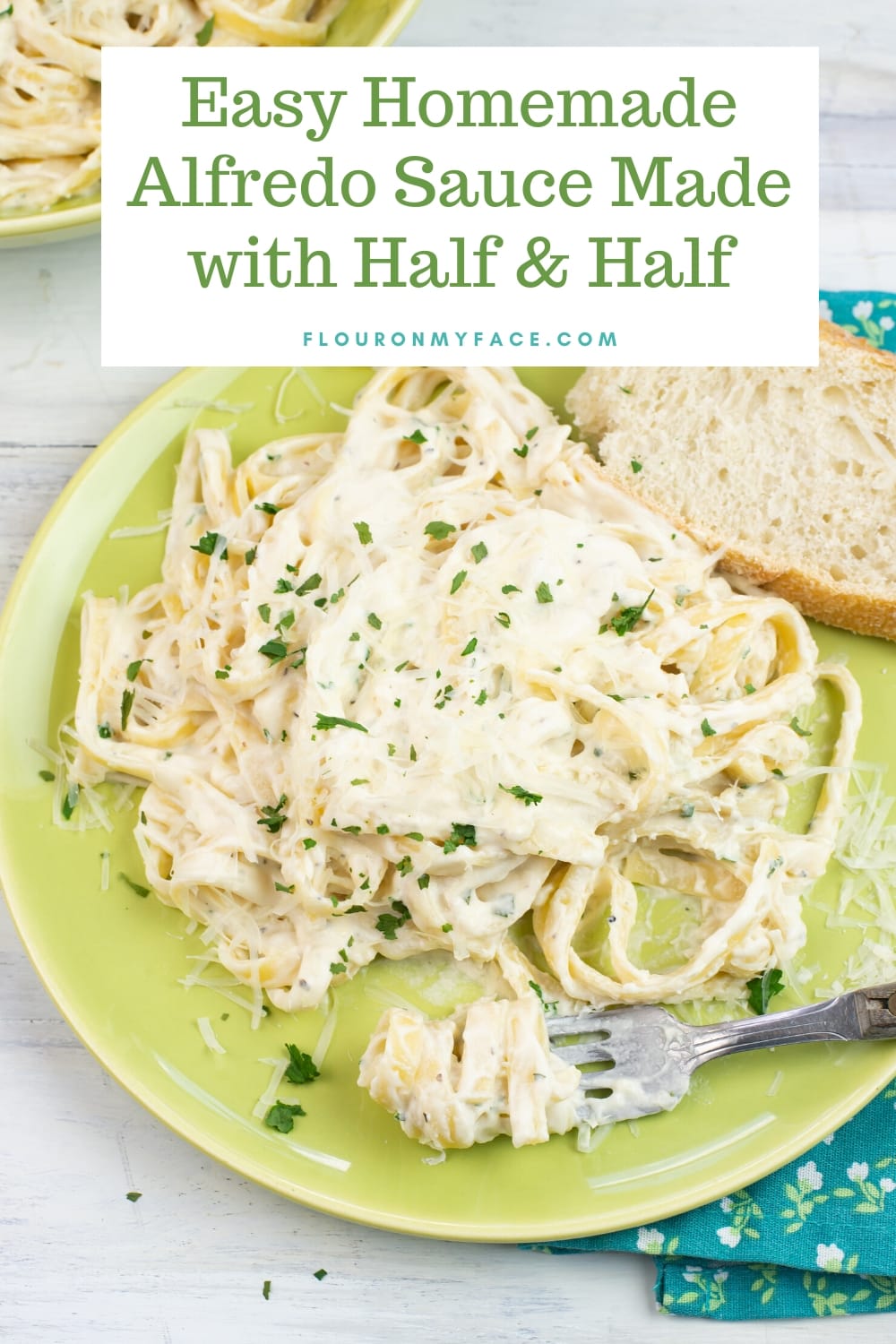 A green dinner plate with a serving of fettuccine Alfredo covered with shredded Parmesan cheese, a sprinkle of parsley. There is a piece of crusty bread on the plate with a fork with a twirl of pasta on it.