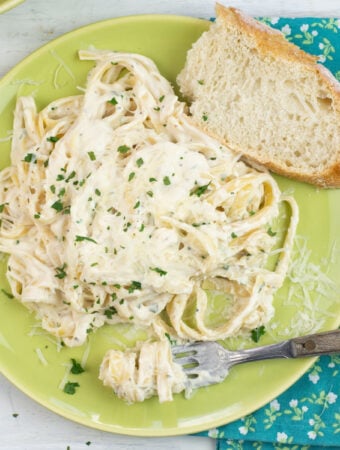 Alfredo Sauce made with half and half on a dinner plate with a slice of crusty bread, cloth napkin and fork