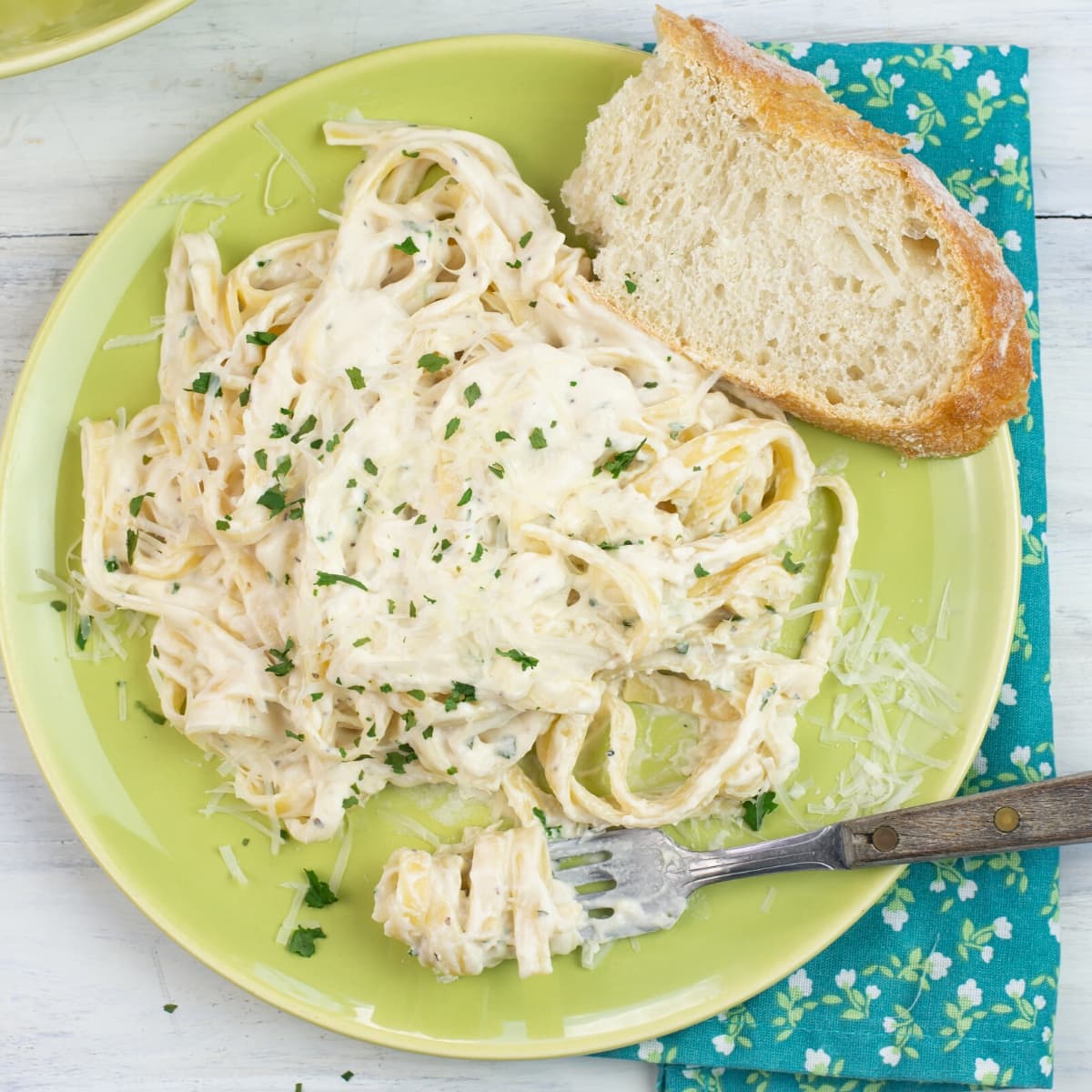 Alfredo Sauce made with half and half on a dinner plate with a slice of crusty bread, cloth napkin and fork