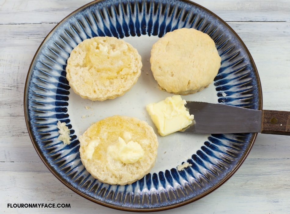freshly baked sourdough biscuits on a plate with melted butter spread over two halves of the warm biscuit.