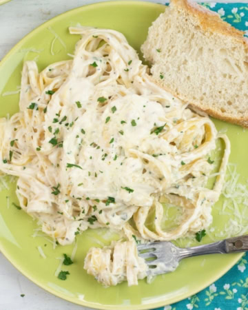 Alfredo Sauce made with half and half on a dinner plate with a slice of crusty bread, cloth napkin and fork