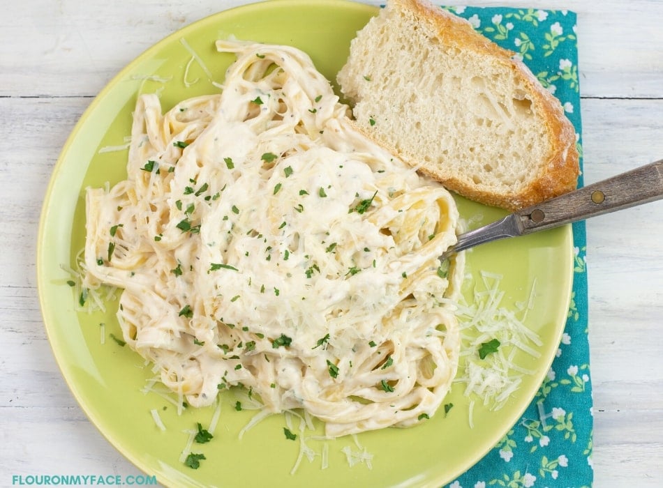 green dinner plate with a serving of Fettuccine Alfredo with a slice of crusty bread on the side