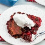 A serving of red velvet dump cake topped with whipped cream.