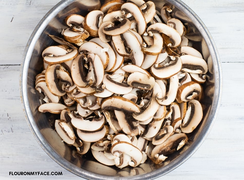 overhead photo of a metal bowl with sliced mushrooms