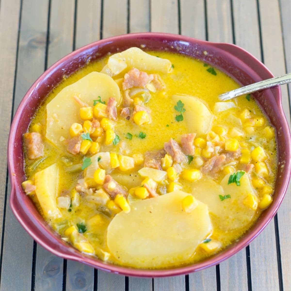 A brown bowl with a serving of cheesy ham and potato soup.