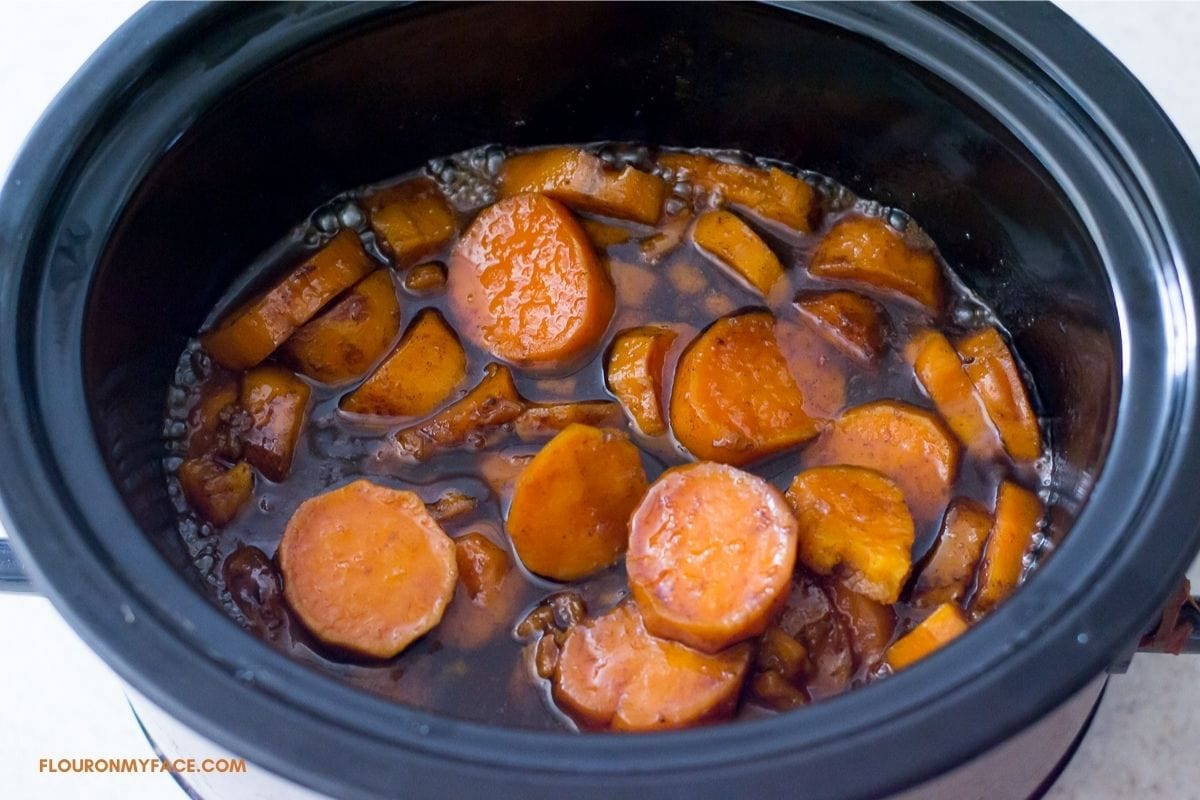 Sliced sweet potatoes covered with a brown sugar glaze in a crock pot..