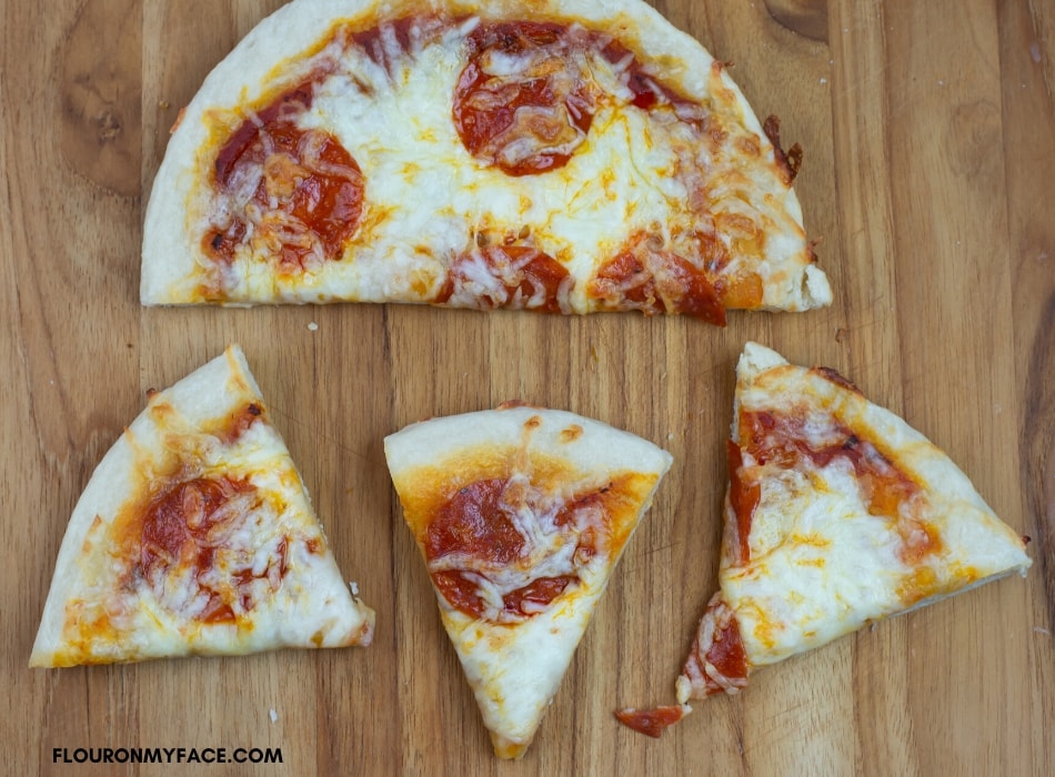 a homemade pepperoni personal pan pizza cut into pieces on a wooden cutting board