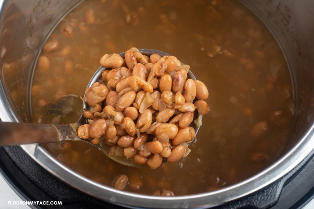 overhead photo of a ladle filled with dried pinto beans that have just finished pressure cooking